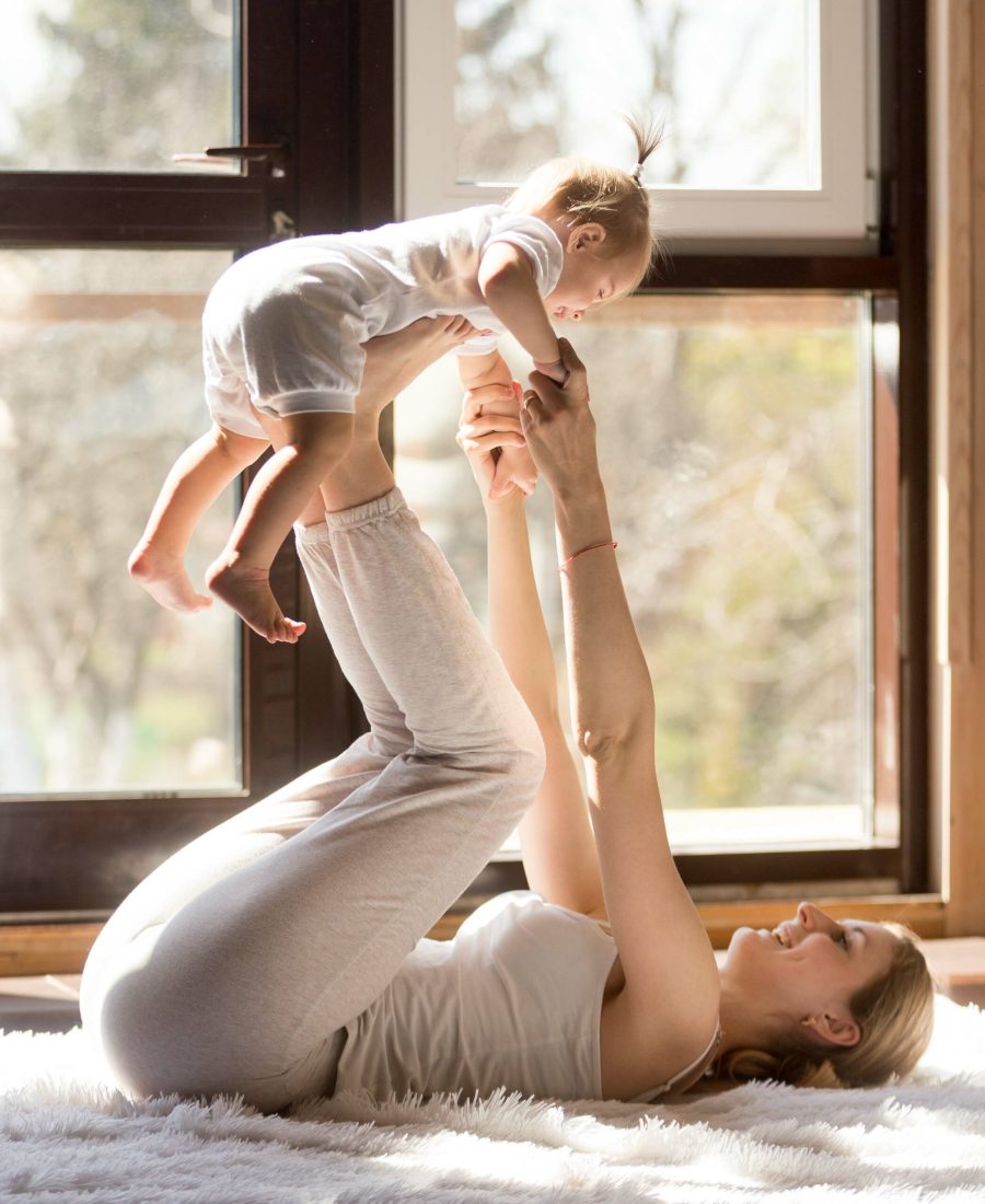 Young attractive sporty mother working out with her baby daughter, exercising at home wearing white sportswear, , leg lifting with baby,  postnatal exercise for abs. Healthy lifestyle concept photo